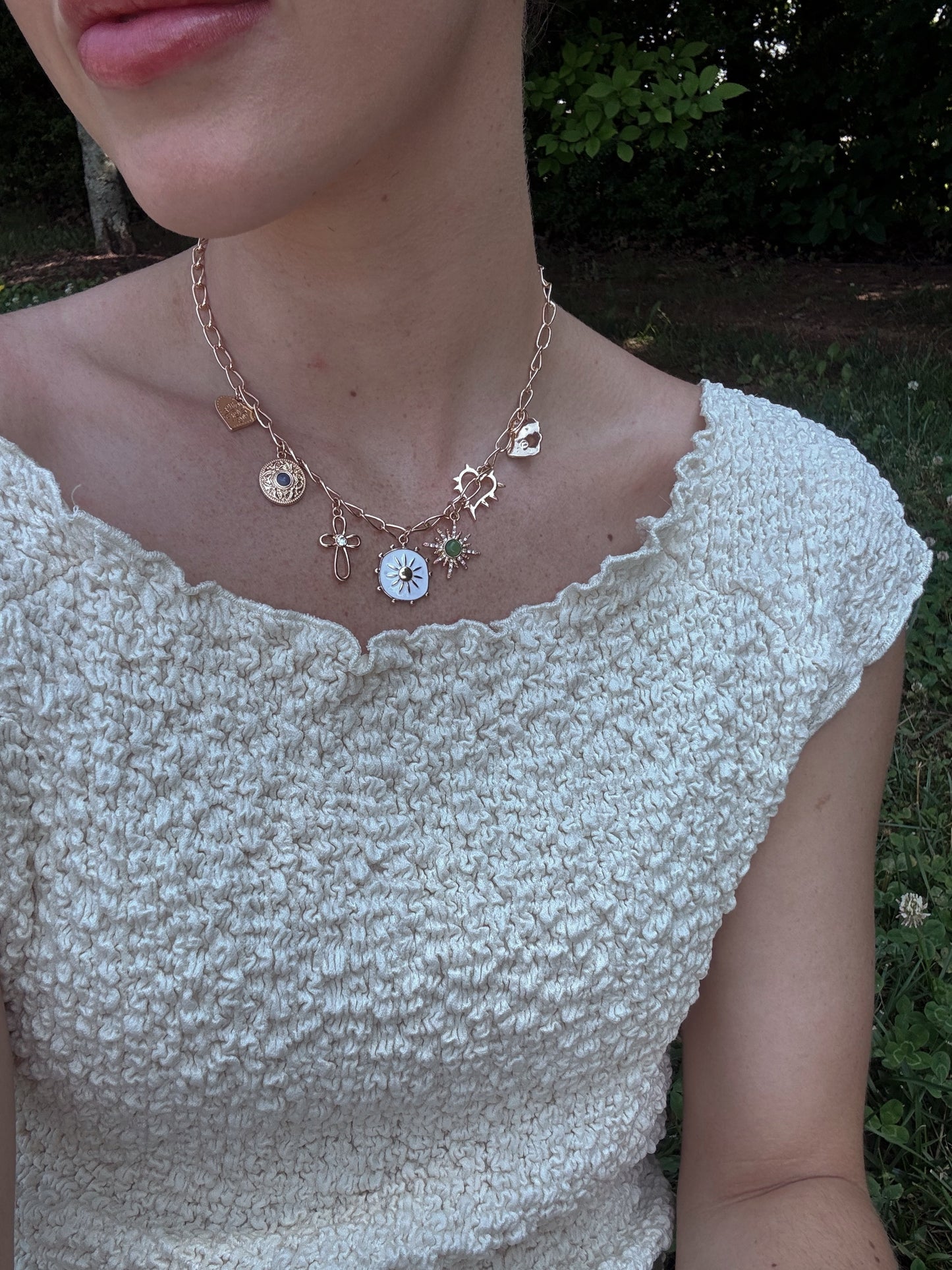 Close-up of a person wearing a charm necklace with a beige crinkle boat neck top