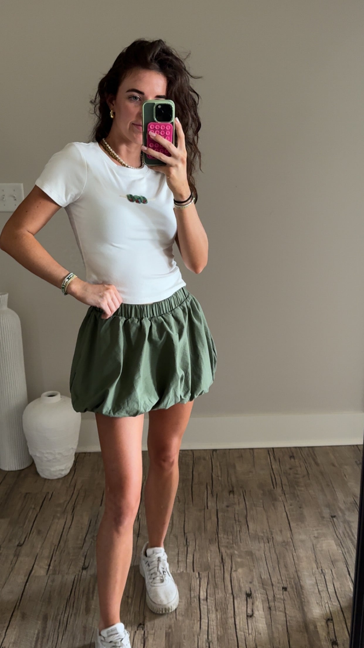 Person wearing a white t-shirt and green skirt indoors.