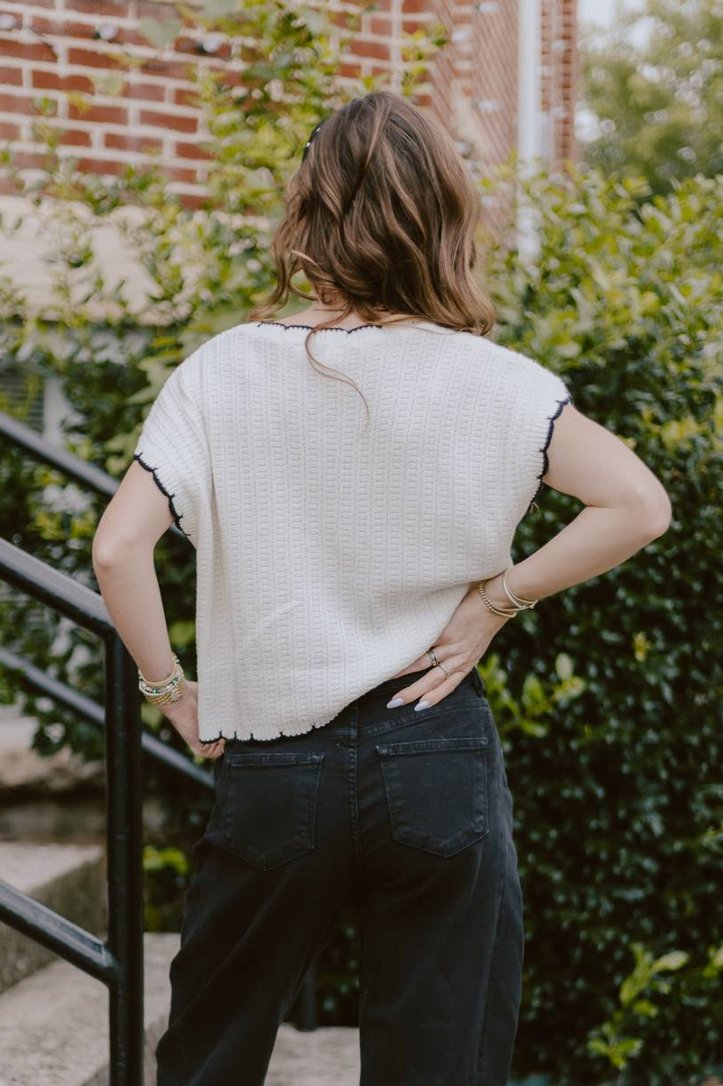 Person wearing a white top and dark jeans standing on steps outdoors.