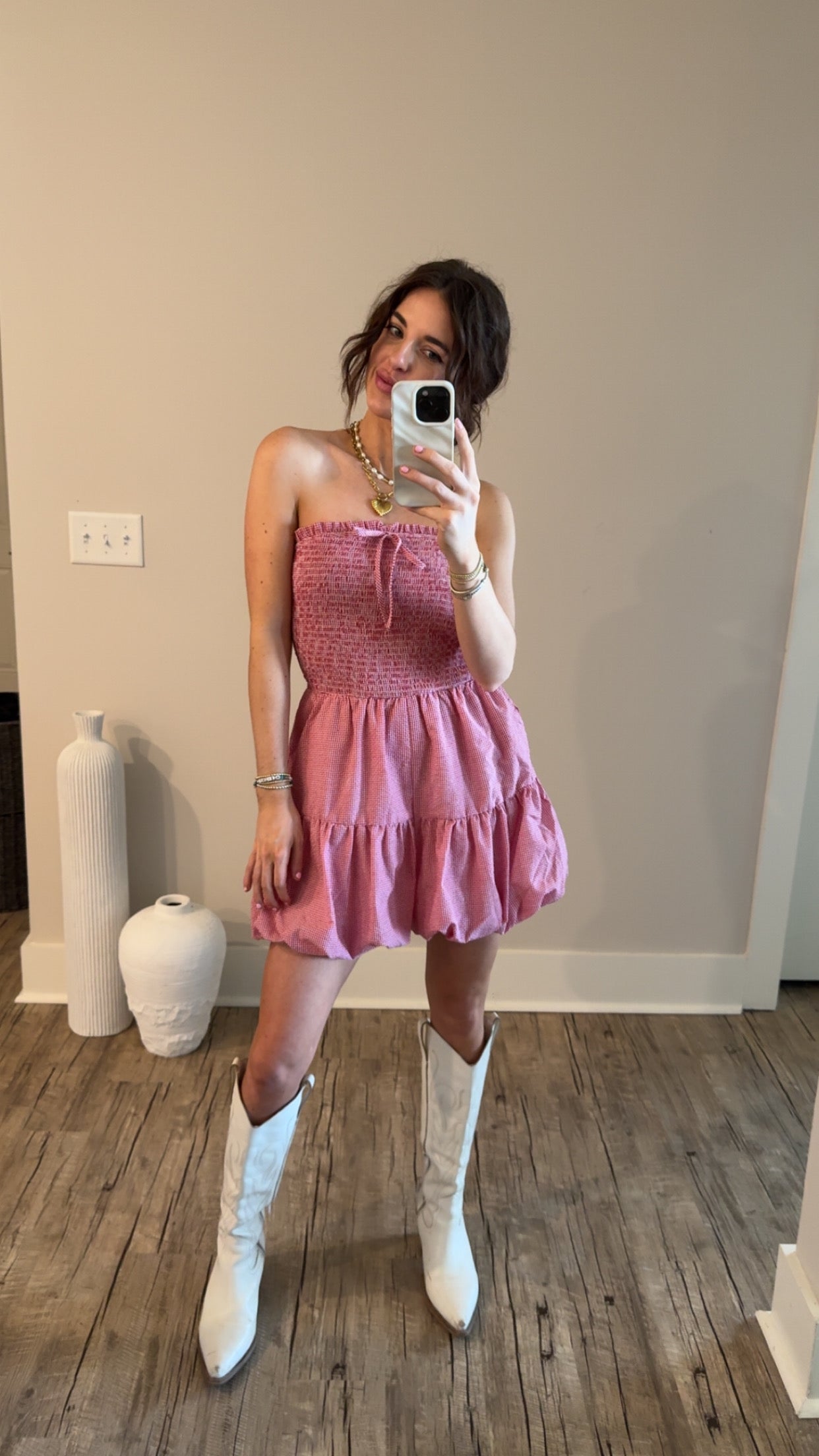 A person wearing a red and white gingham strapless romper with a bubble hem, paired with white cowboy boots.