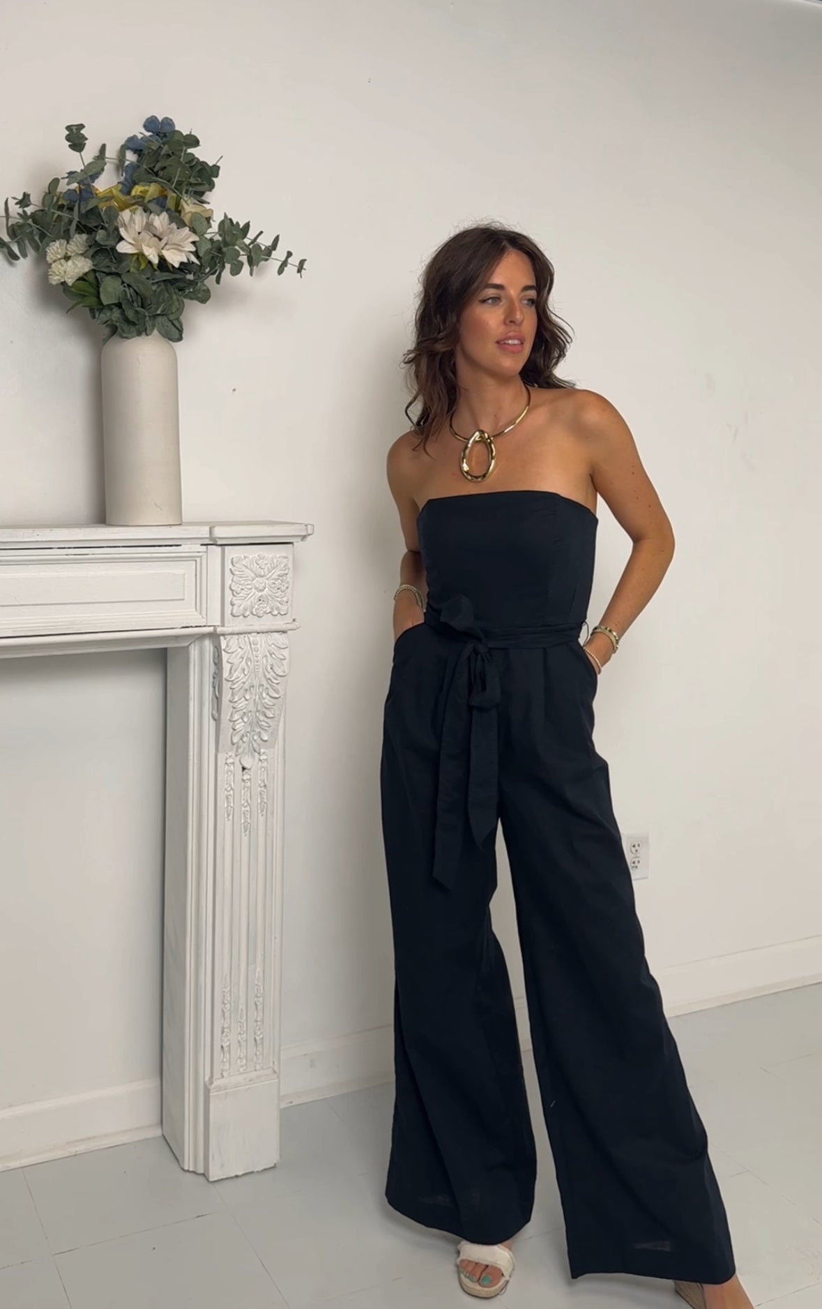 Navy strapless jumpsuit standing in a room with a white wall and decorative elements.
