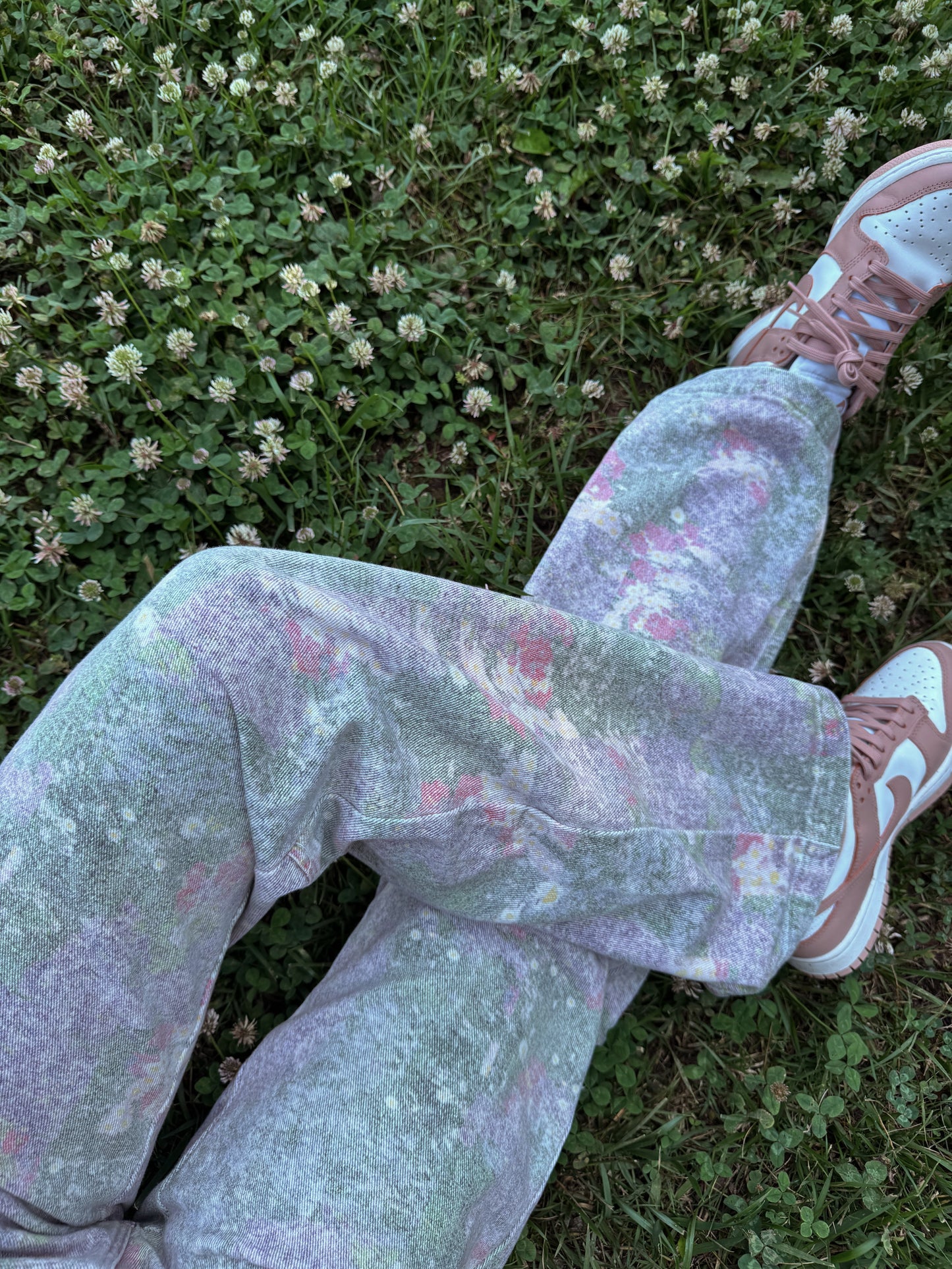Person wearing lavender floral straight leg pants with a floral pattern lying on grass.