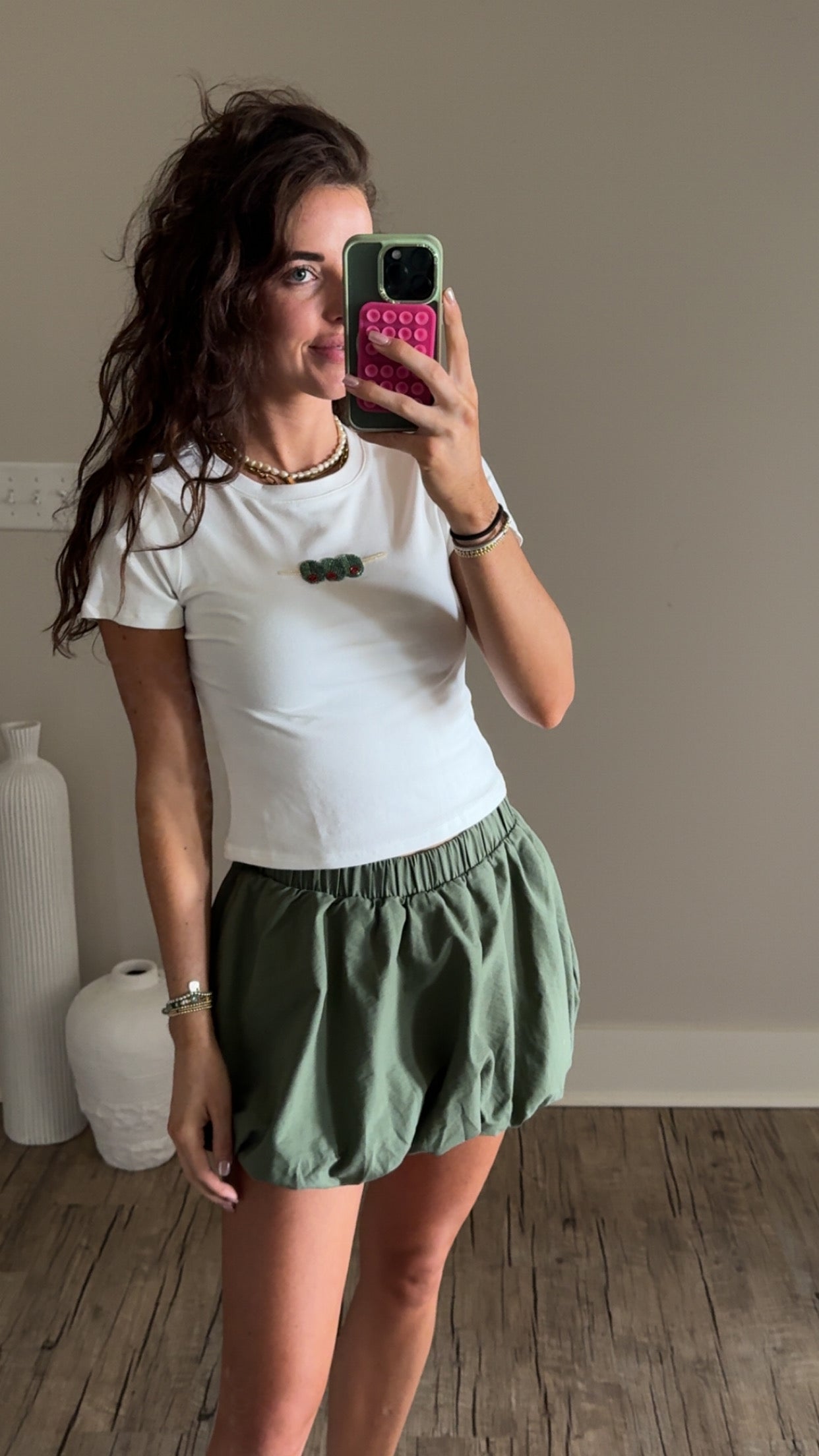 A person wearing an olive green skirt with an elastic waistband and a bubble hem, paired with a white t-shirt.