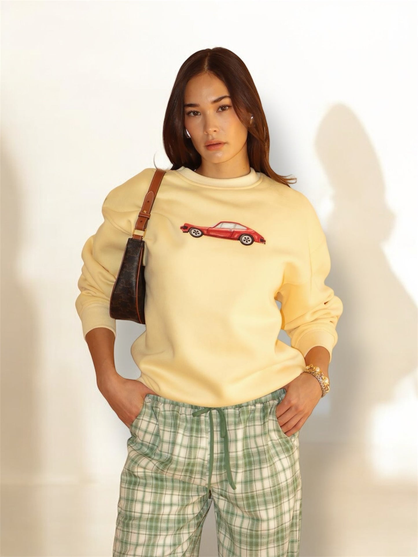 A person wearing a yellow sweatshirt with a graphic of a red car on it.