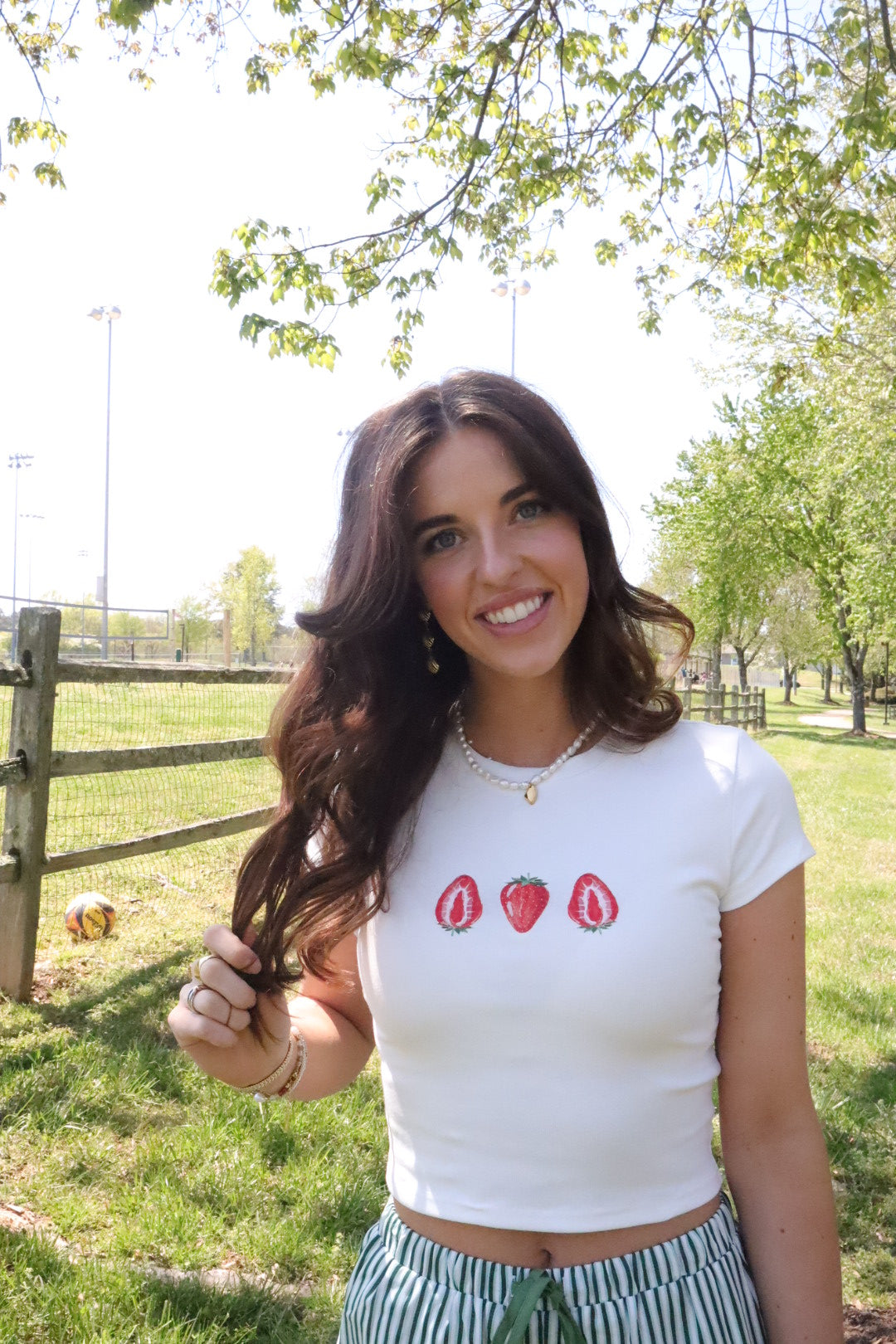 This image features a delightful white tee shirt adorned with a charming strawberry embroidery at the chest area. The shirt is designed to fit snugly, emphasizing a cropped look that is currently fashionable.
