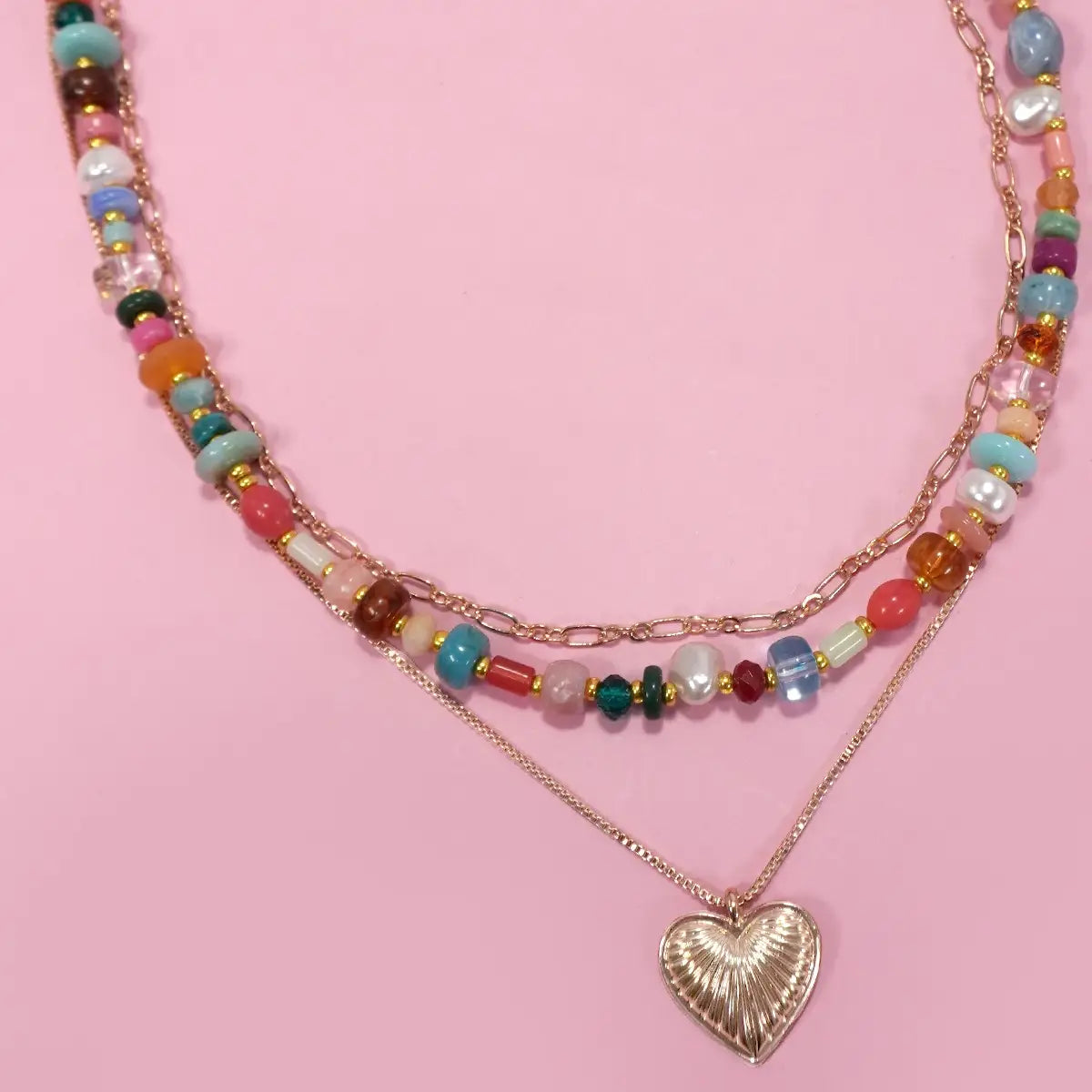 colorful beaded necklace stacked with pendent and gold chain on pink background