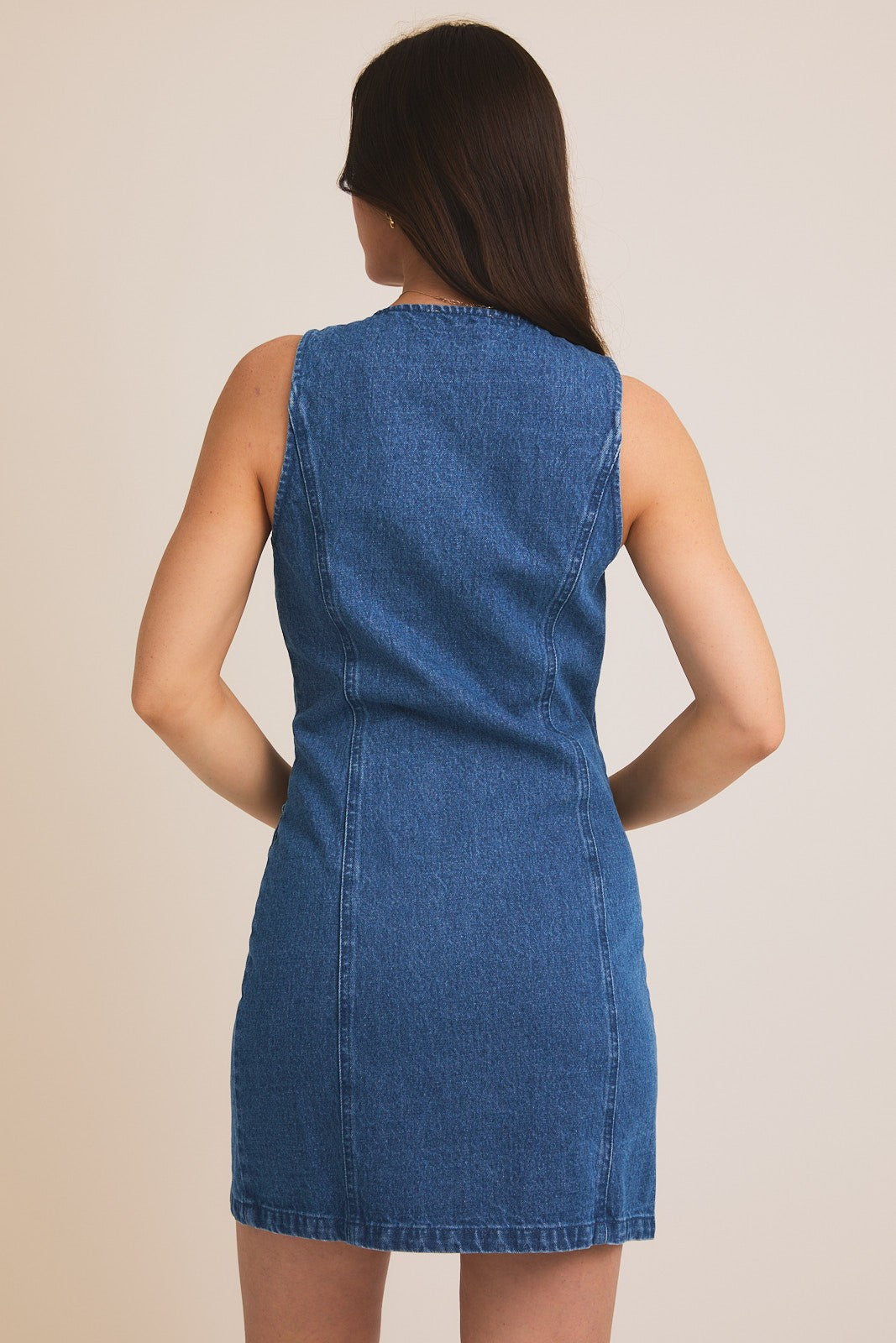Woman showing back of a blue denim dress against a beige background