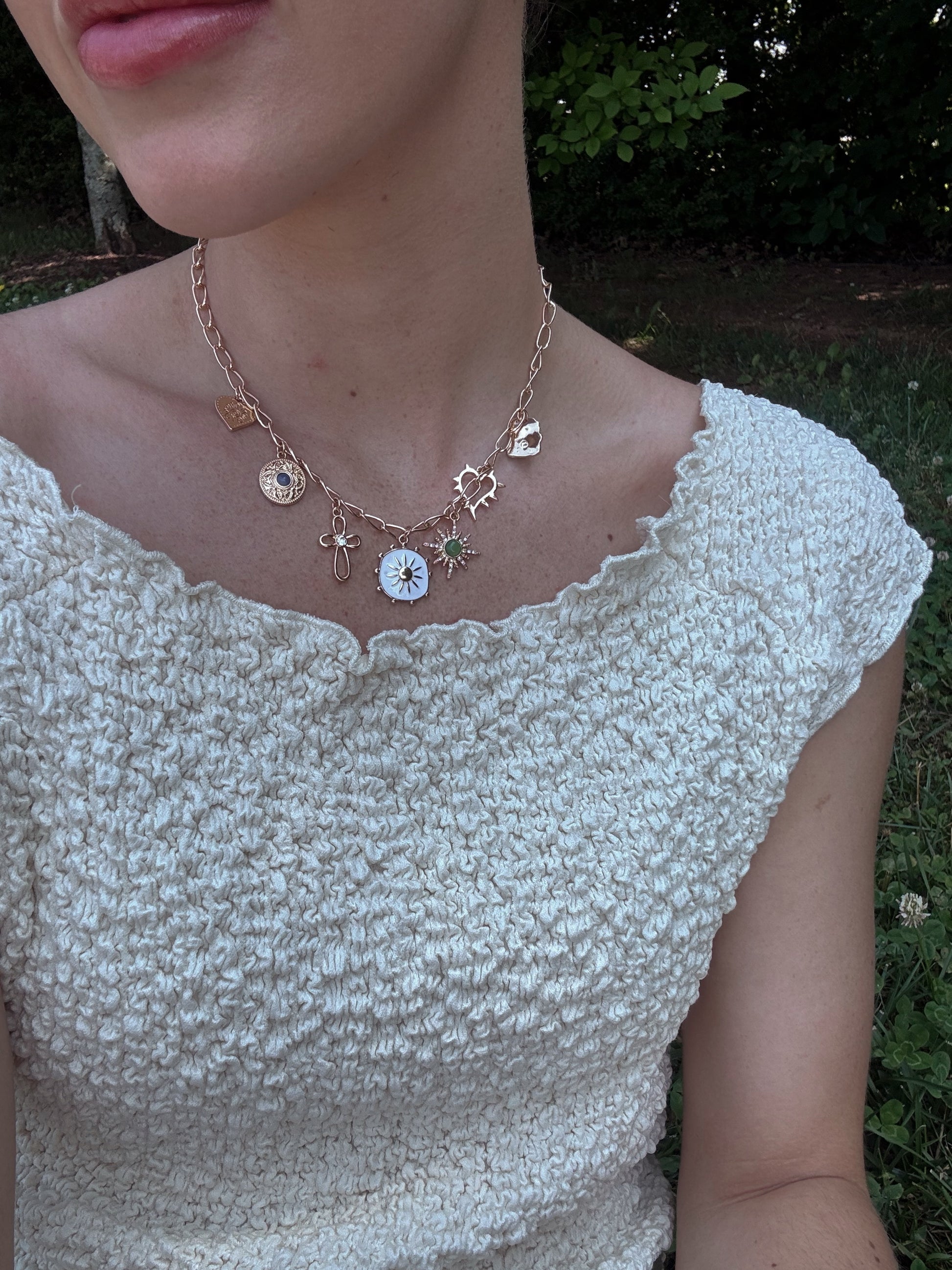 Close-up of a person wearing a charm necklace with a beige crinkle boat neck top