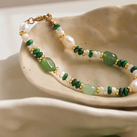 A bracelet with green stone beads and gold-colored accents displayed on a beige ceramic dish.