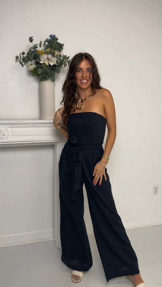 Navy blue strapless jumpsuit standing in a room with a white wall and decorative vase.