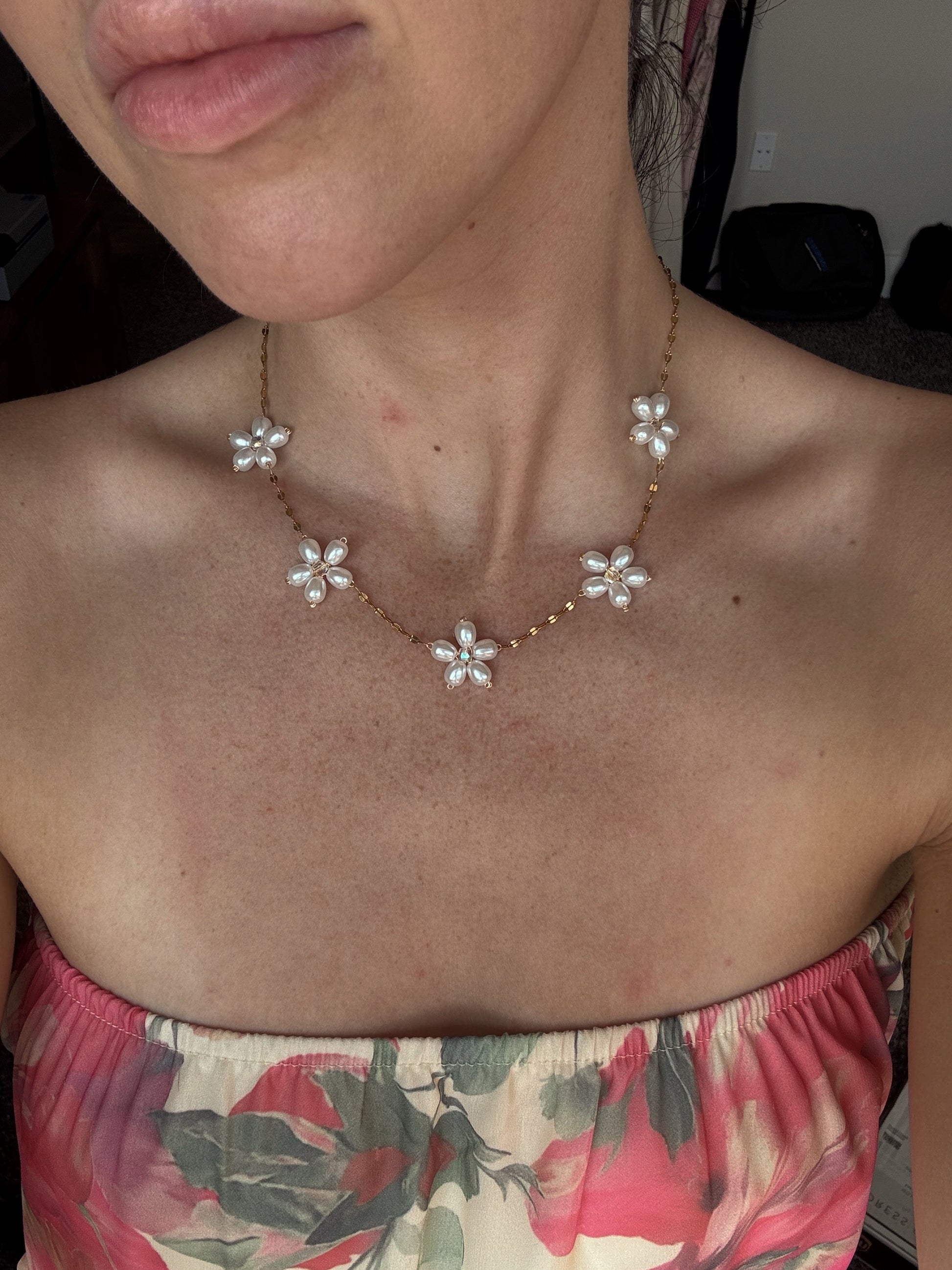 gold Necklace with floral pendants worn by a person in a floral top.