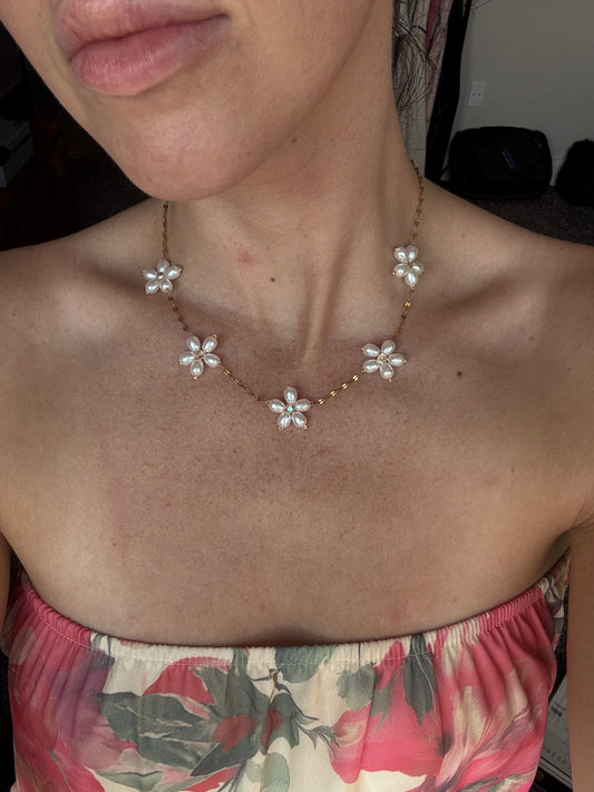 gold Necklace with floral pendants worn by a person in a floral top.