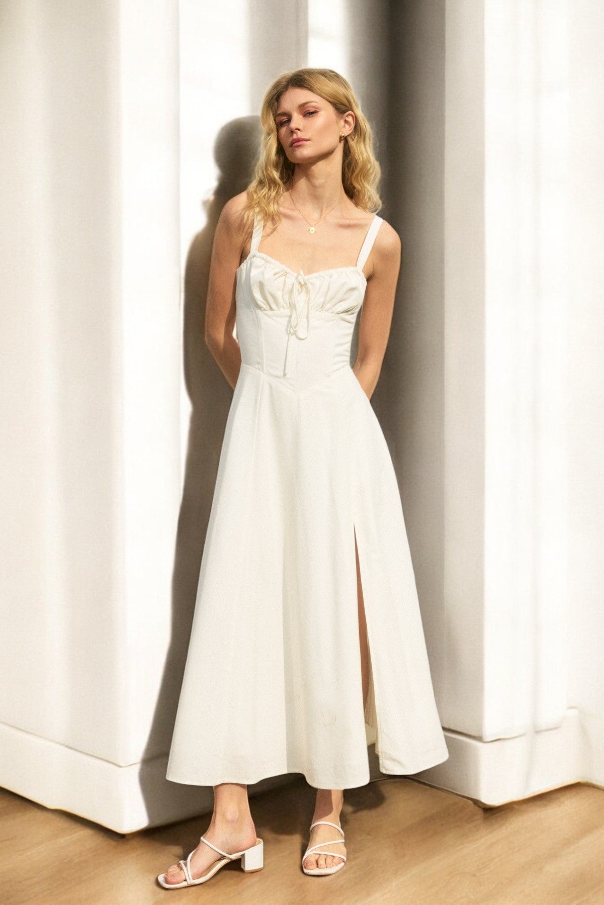 A woman modeling a white sweetheart neckline corset bodice midi dress with lace up back and fit & flare silhouette. She is wearing the dress with a pair of heels.