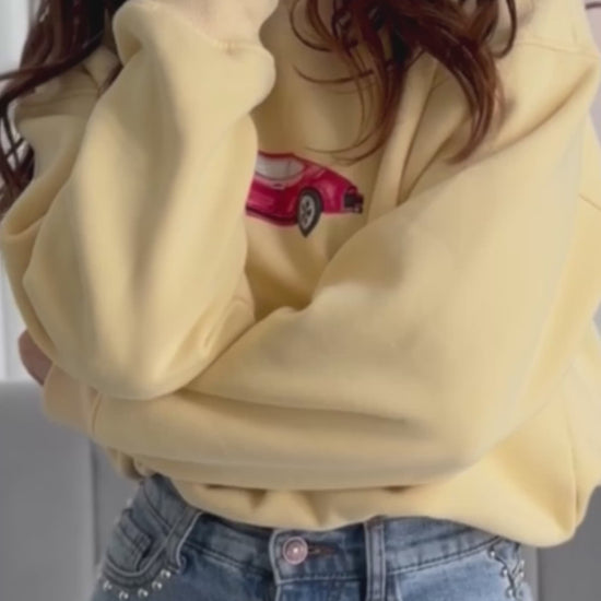 video of person wearing butter yellow crewneck sweater with vintage red car graphic on it
